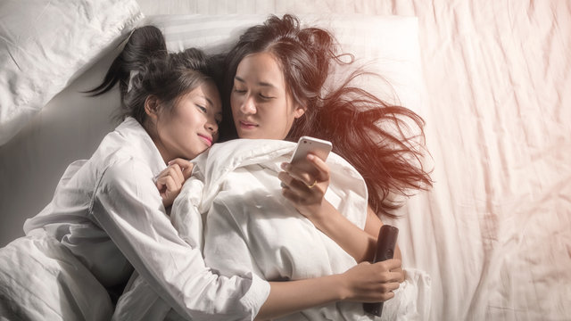 Photo of two girls were playing a smart phone on relaxing moment on bed in holiday . Shows that the technology has already spread to all areas. That mean , all people can work by smart phone at home.