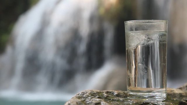 ice cube falls into a glass of water on the background of Waterfall in forest