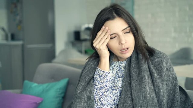 Sick woman coughing sitting covered with blanket on sofa at home
