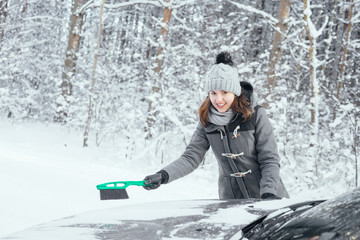 Fototapeta na wymiar Happy girl cleaning her car of snow in the winter