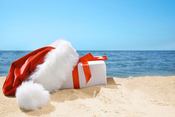 Gift box with Santa hat on beach. Christmas holiday concept