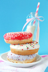 Plate with stack of delicious donuts and blurred bottle of milk on blue background