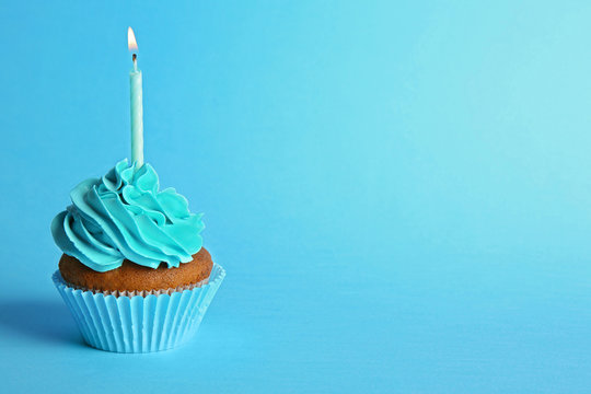 Fresh tasty cupcake with candle on blue background