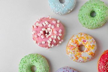 Tasty donuts with colorful sprinkles on light background