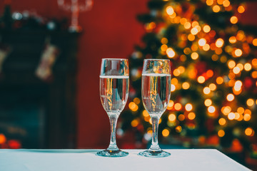 Beautiful two glasses of champagne standing on the table in the background of a blurred room with a decorated Christmas tree and fireplace. Soft focus. Shallow DOF