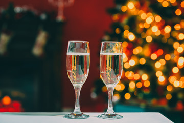 Beautiful two glasses of champagne standing on the table in the background of a blurred room with a decorated Christmas tree and fireplace. Soft focus. Shallow DOF