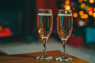 Beautiful two glasses of champagne standing on the table in the background of a blurred room with a decorated Christmas tree and fireplace. Soft focus. Shallow DOF