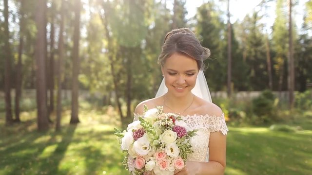 An incredibly beautiful bride in the spruce forest with a bouquet of flowers.