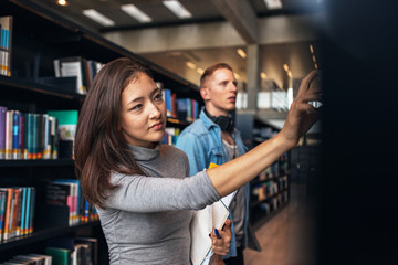 Obraz na płótnie Canvas University students taking book from shelf in library