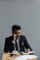 A beautiful successful man talking on phone office and writing in a notebook in cafe