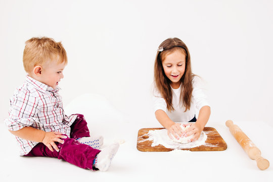 Children cooking bakery. Girl kneading dough for pastry, her little brother sitting on kitchen table, free space on white. Homemade bakery, kids culinary, sweet making concept