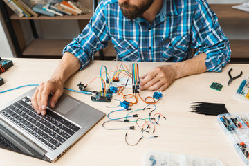Programmer testing his new invention on laptop. Workplace of hacker, working with electronic...