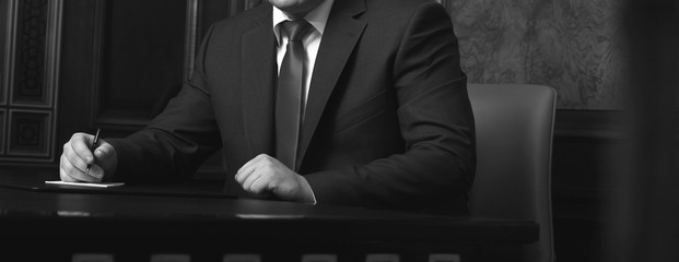 Close up of businessman sitting at table and signing document, black and white photo