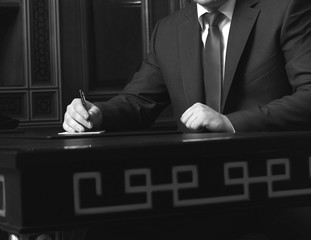 Close up of businessman sitting at table and signing document, black and white photo