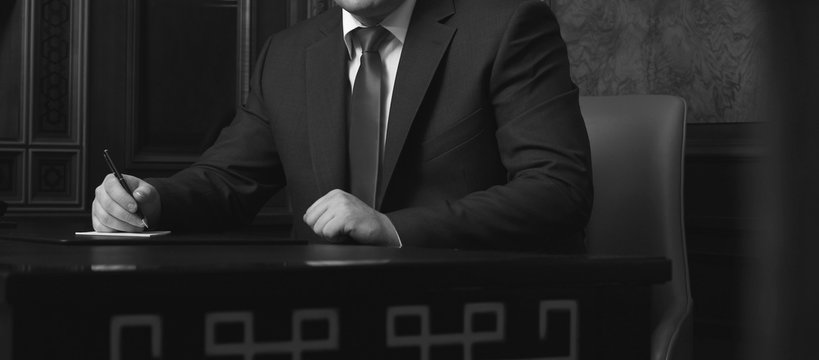 Close up of businessman sitting at table and signing document, black and white photo