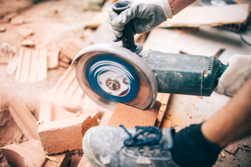 worker using grinder on construction site for cutting bricks, debris. Tools and bricks on new...