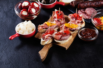 Spanish tapas with slices jamon serrano and grilled pepper. Also olives, salami, pickled onions, and peppers stuffed with cheese