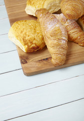 Freshly baked croissants and bread rolls arranged on a wooden background 