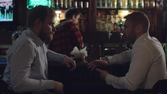 Two businessmen talking at the bar counter while bartender working in the background