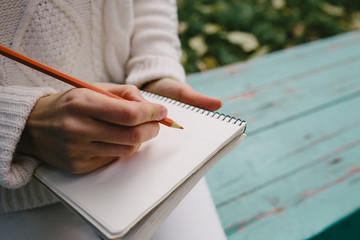 woman draws a colored pencil in a notebook outdoor. Close up of open pad in female hands with pen sitting on stairs in the park