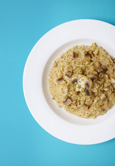 A dish of chicken and mushroom risotto on a bright blue background