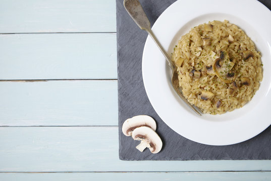 A bowl full of chicken and mushroom risotto on a rustic wooden table top background forming a page border