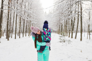 Fototapeta na wymiar Mother and little toddler girl walking in the winter forest and having fun with snow. Family enjoying winter. Christmas and lifestyle concept.