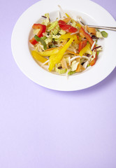 A bowl of fresh stir fry vegetables on a pastel purple background forming a page border