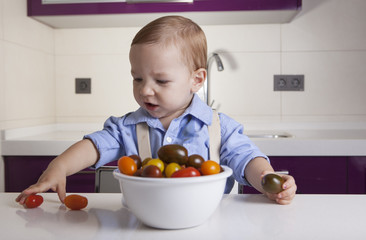 Baby boy playing with ripe colorful cherry tomatoes