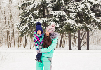 happy mother holding baby girl on the walk in winter snowy forest