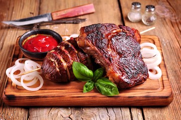 Delicious juicy beef ribeye steak with baked eggplant with bacon, onion on a wooden board. Rustic style.