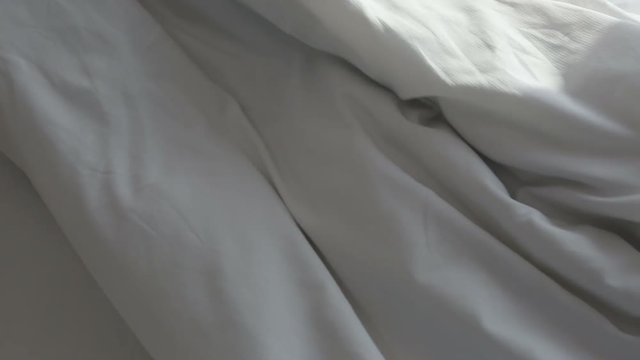 white blanket on bed being pulled slowly out of frame
