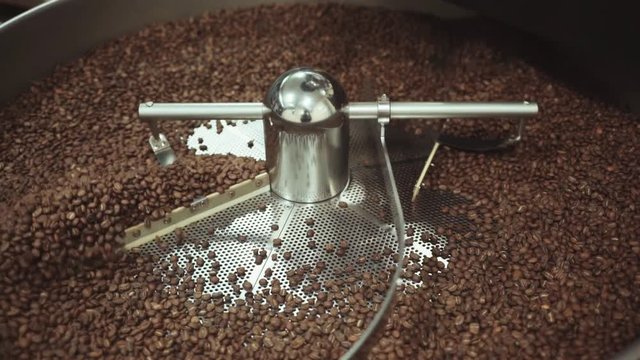 Traditional roaster machine mixing freshly roasted coffee beans at the local coffee shop. Close up view, slow motion.