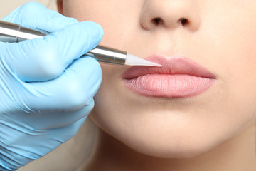 Cosmetologist making permanent  make up on lips, close up