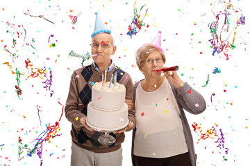 Senior couple with horns and party hats celebrating birthday - Powered by Adobe