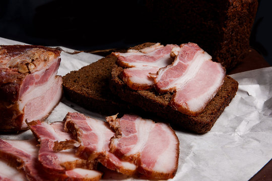 Puff smoked bacon with rye black bread on the packaging paper. V