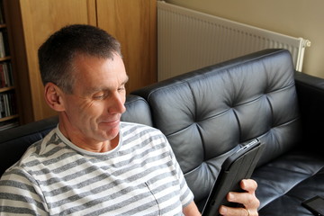 Fototapeta premium Happy older man finding something amusing on his tablet computer