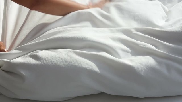 closeup of woman throwing white blanket on bed
