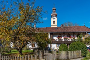 Fototapeta premium Bauernhaus mit Holzgartenzaun, Baum und Kirchturm in Bayern