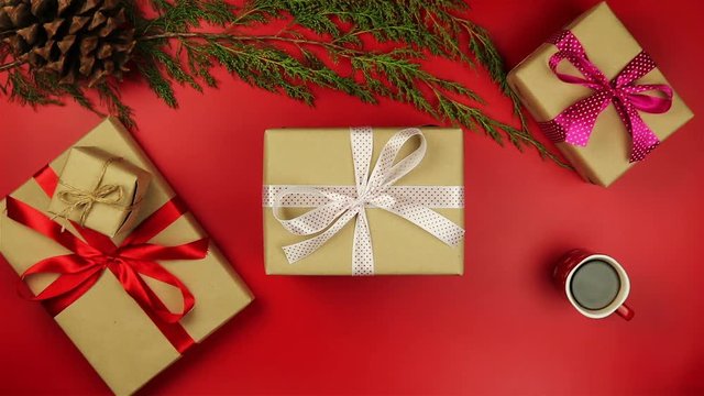 Top view hands holding christmas presents on red background from above. Gift wrapped in brown paper and tied white ribbon