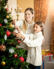Obraz na płótnie Canvas Portrait of smiling girl helping mother decorating Christmas tre