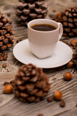 Small white cup of coffee, cocoa beans, hazelnuts, cone on wooden background