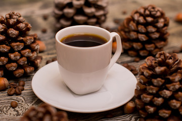 Small white cup of coffee, cocoa beans, hazelnuts, cone on wooden background