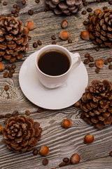 Small white cup of coffee, cocoa beans, hazelnuts, cone on wooden background