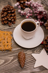 Small white cup of coffee, cocoa beans, hazelnuts, cookies, cone, christmas decoration, fir branch in snow on wooden background
