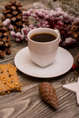 Small white cup of coffee, cocoa beans, hazelnuts, cookies, cone, christmas decoration, fir branch in snow on wooden background