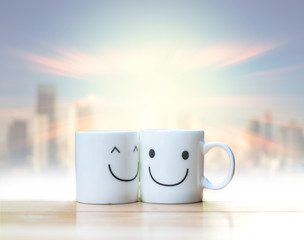 Two happy cups on abstract Blurred photo of cityscape with sun b