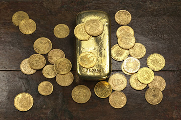 various European circulation gold coins from the 19th/20th century around a gold bar on rustic wooden background