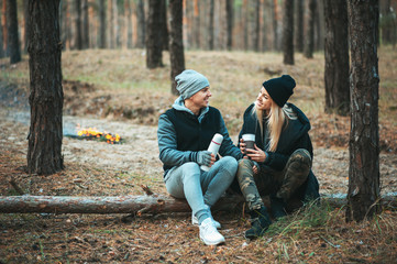Romantic couple sitting near bonfire, autumn forest background. Young blonde woman and handsome man. Concept - family, togetherness, love, friendship.