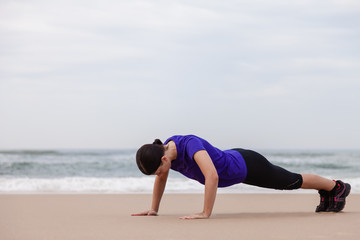 Female athlete executing push-ups at the beach on an Autumn day.